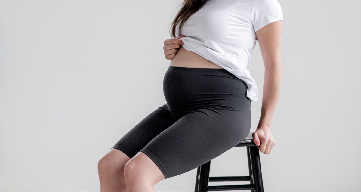 Pregnant woman in cropped maternity leggings and soft top at home, warm natural light