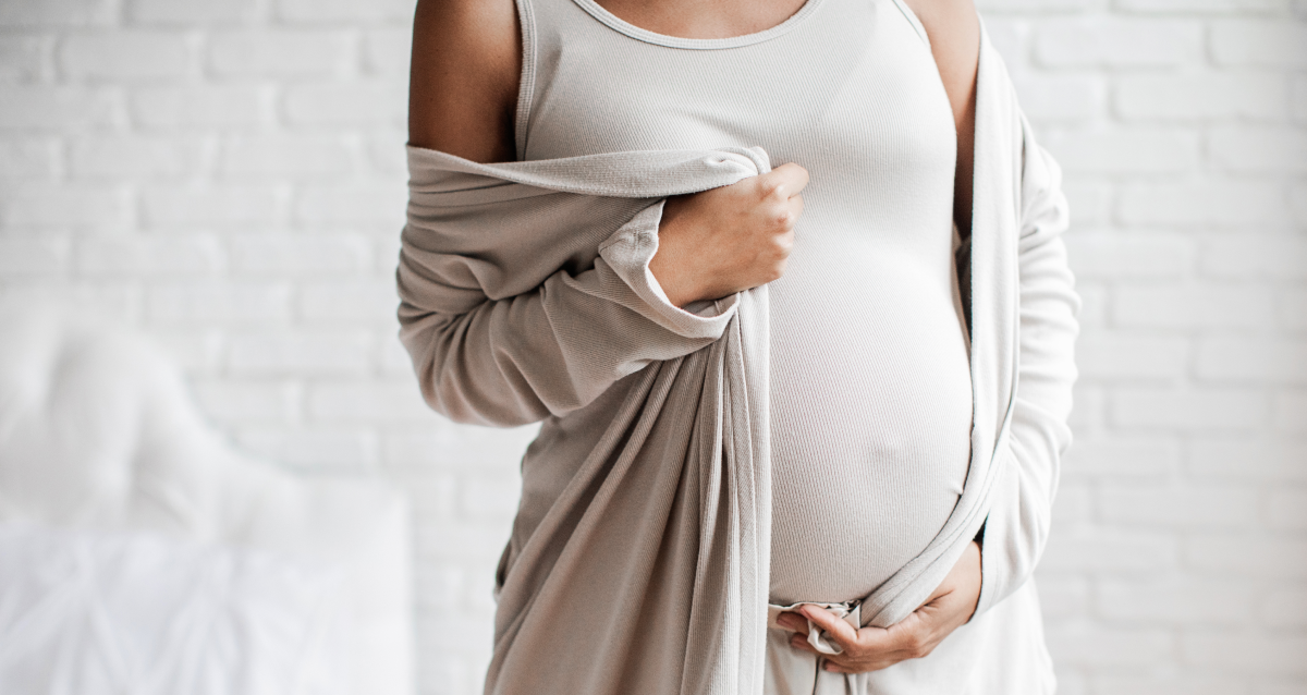 Pregnant woman lounging at home in French terry maternity overalls with spandex, styled with cozy fall layers.
