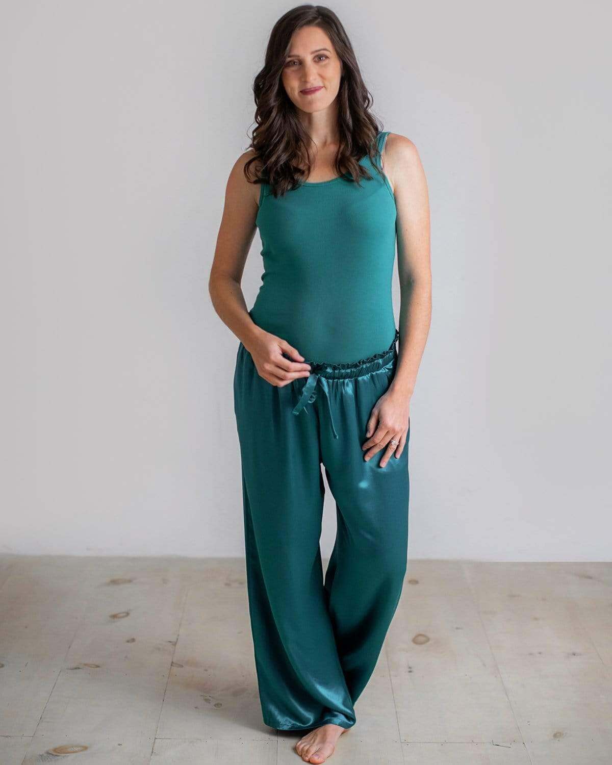 A pregnant woman wearing green satin maternity pajama pants with a paper bag style waistband and a drawcord.