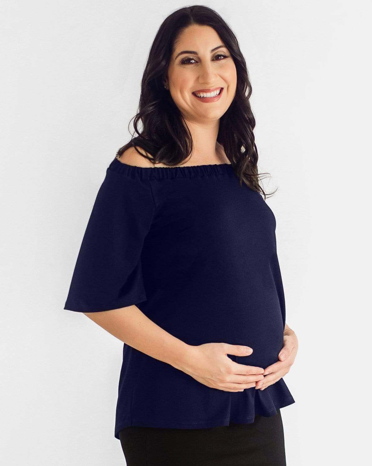 A pregnant woman wearing an off-the-shoulder white maternity top with short sleeves and a ruched neckline.