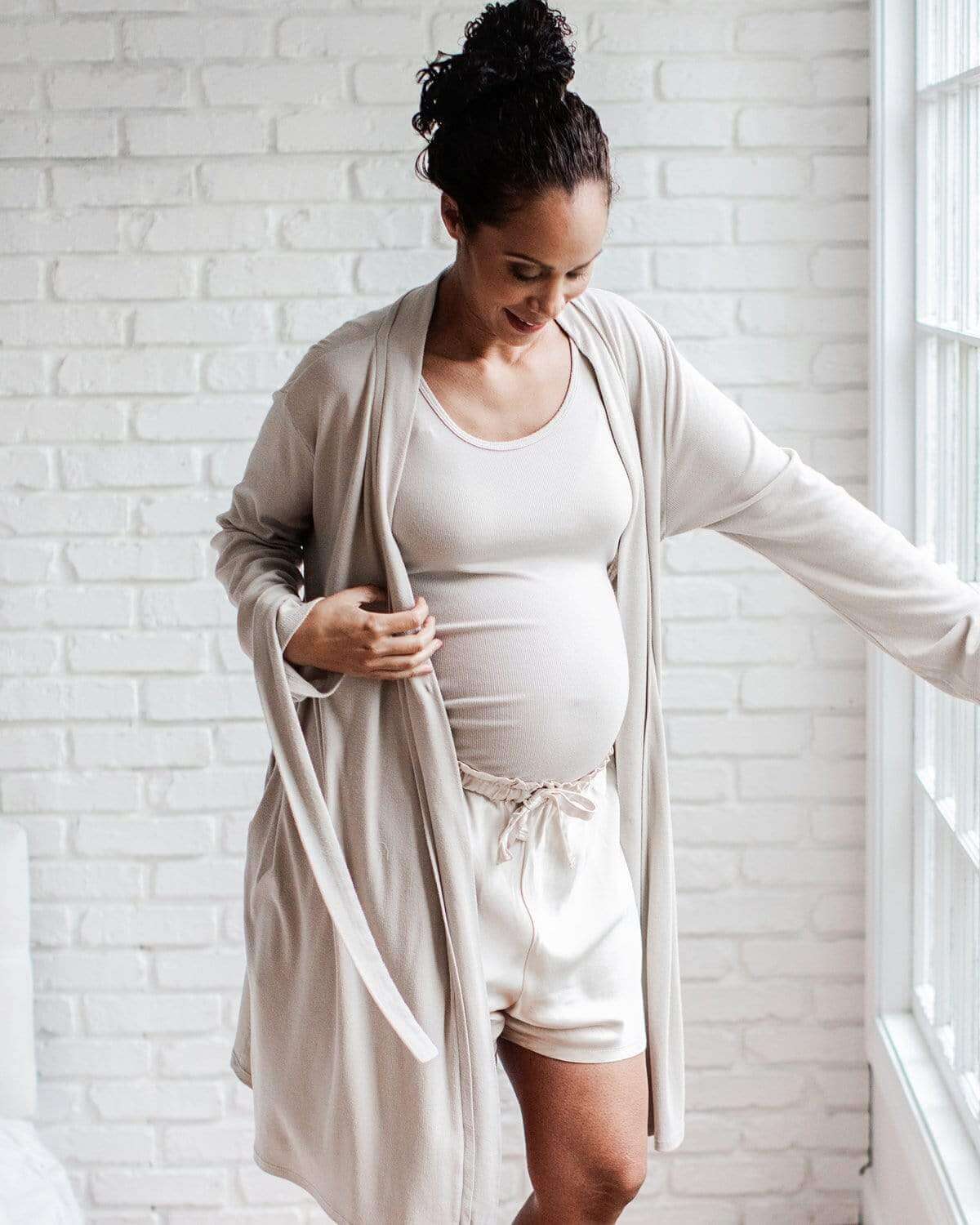 A pregnant woman wearing black satin maternity sleep shorts with a functional drawcord waistband.