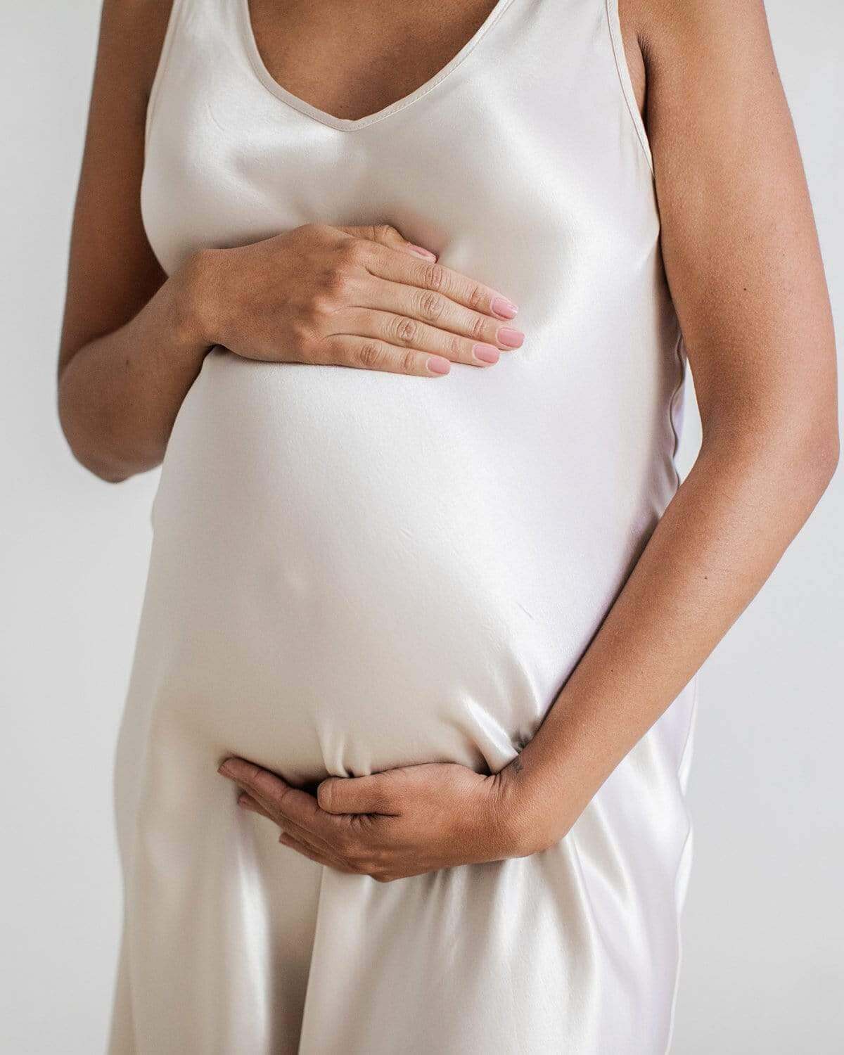 A pregnant woman wearing a green sleeveless maternity nightgown with a V-neck.