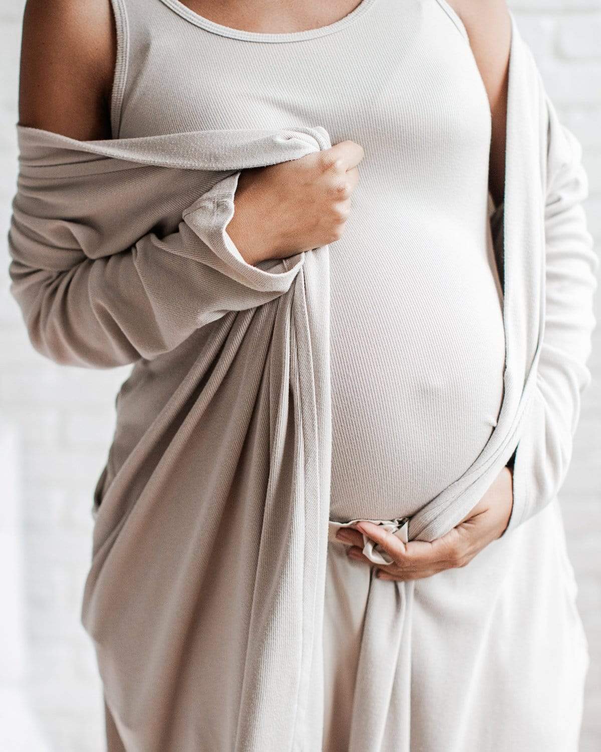 A pregnant woman wearing a long, black, soft rib maternity robe with side seam pockets and a dual position belt.