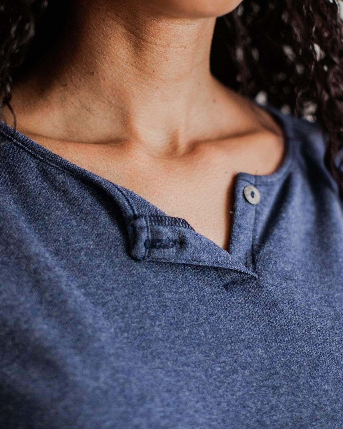 A pregnant woman wearing a black bamboo maternity henley with long dolman sleeves and a mini button placket.