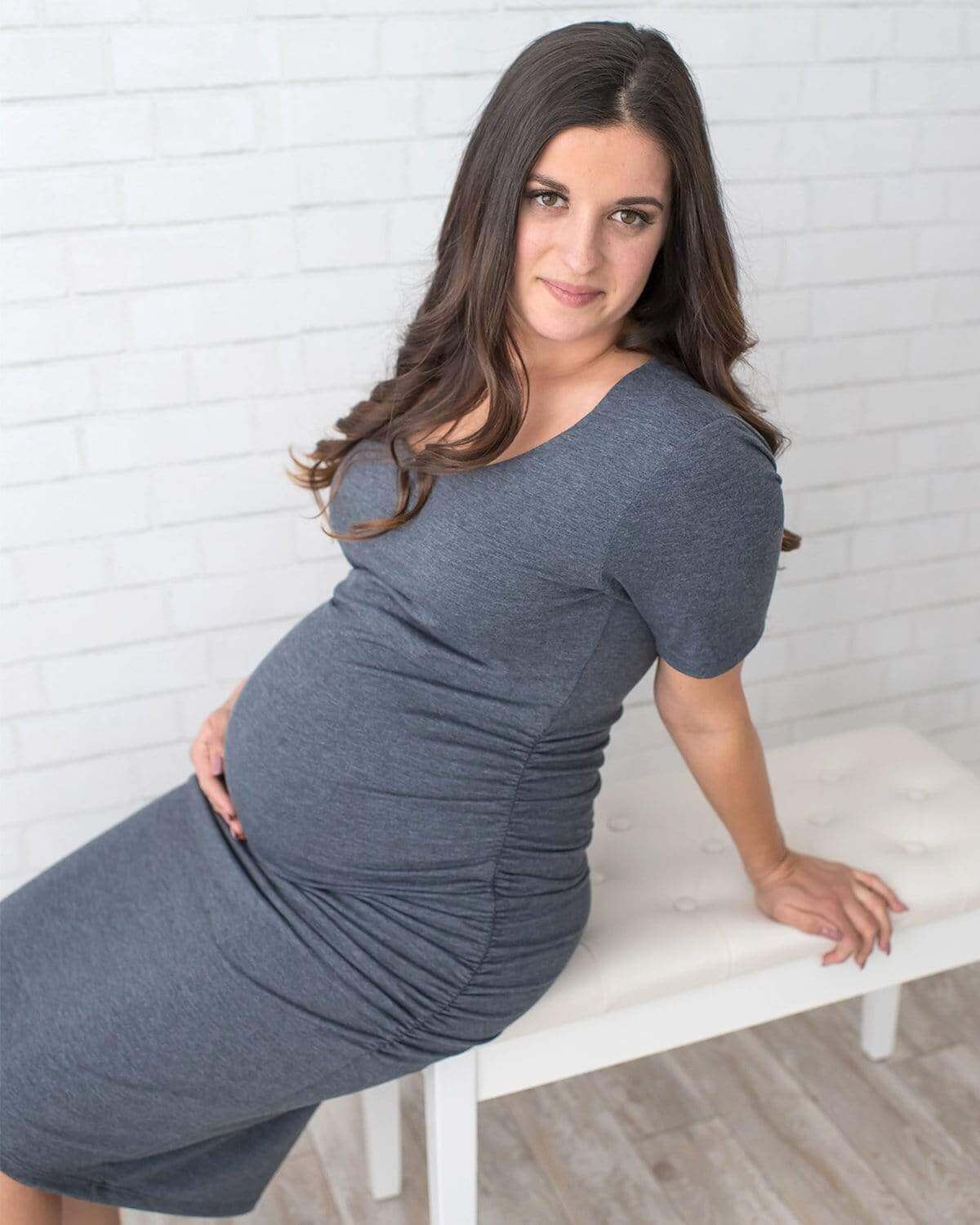 A pregnant woman wearing a short-sleeved, knee-length black maternity dress with side ruching.