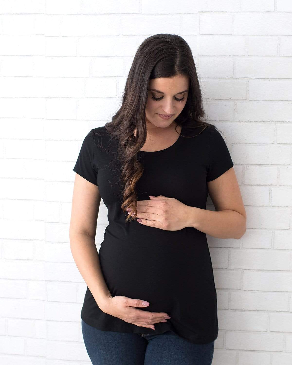 A pregnant woman wearing a black short sleeve maternity tee with a scoop neck.