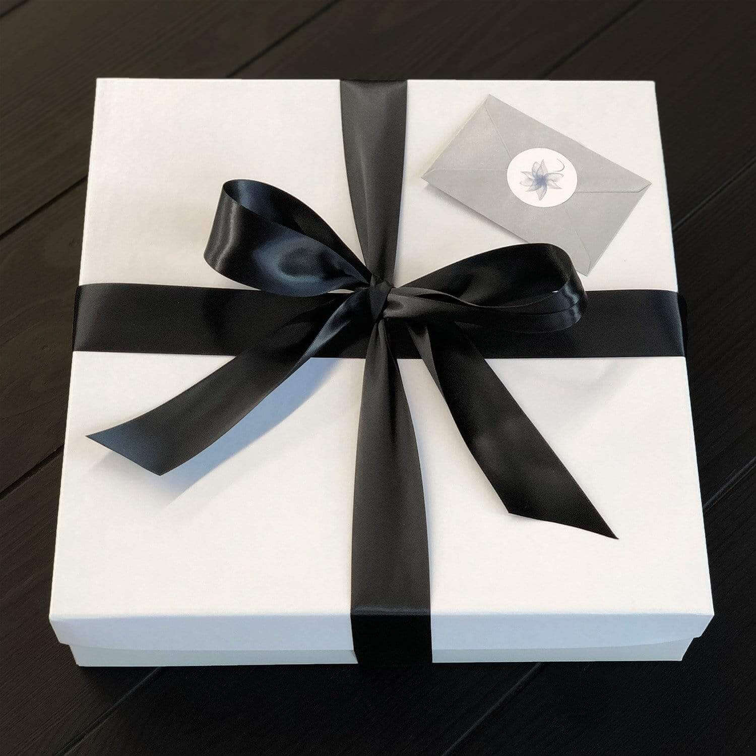A white gift box with a black ribbon bow on top and a silver gift tag attached to the box.