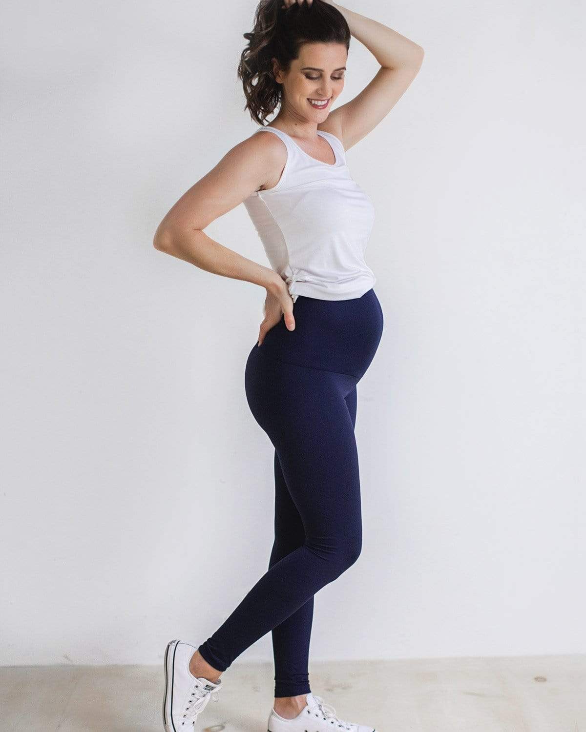 A pregnant woman wearing black full-length maternity leggings with a comfort belly panel, paired with a white top.
