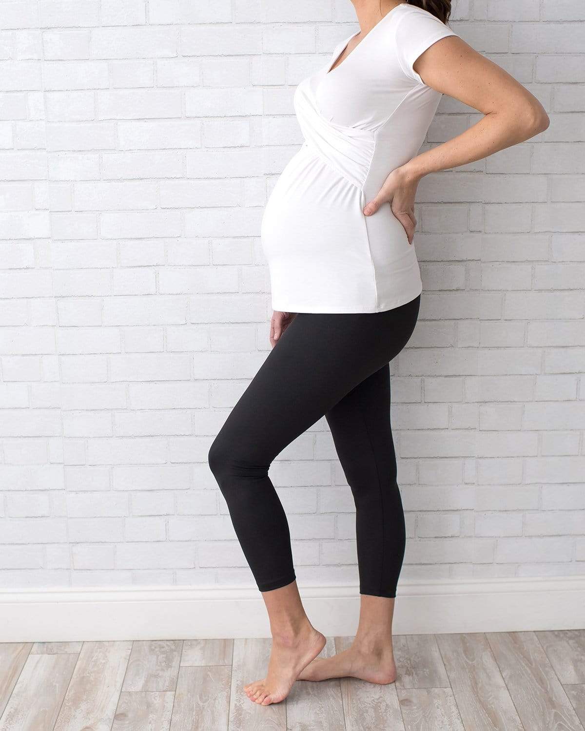 A pregnant woman wearing navy blue ankle-length maternity leggings with a comfort belly panel, standing against a plain background.