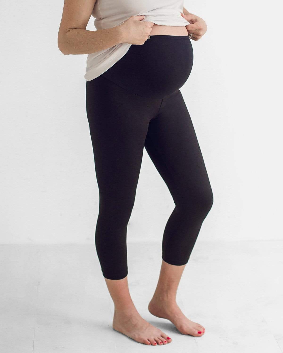 A pregnant woman wearing a white t-shirt and black cropped maternity leggings with a comfort belly panel.