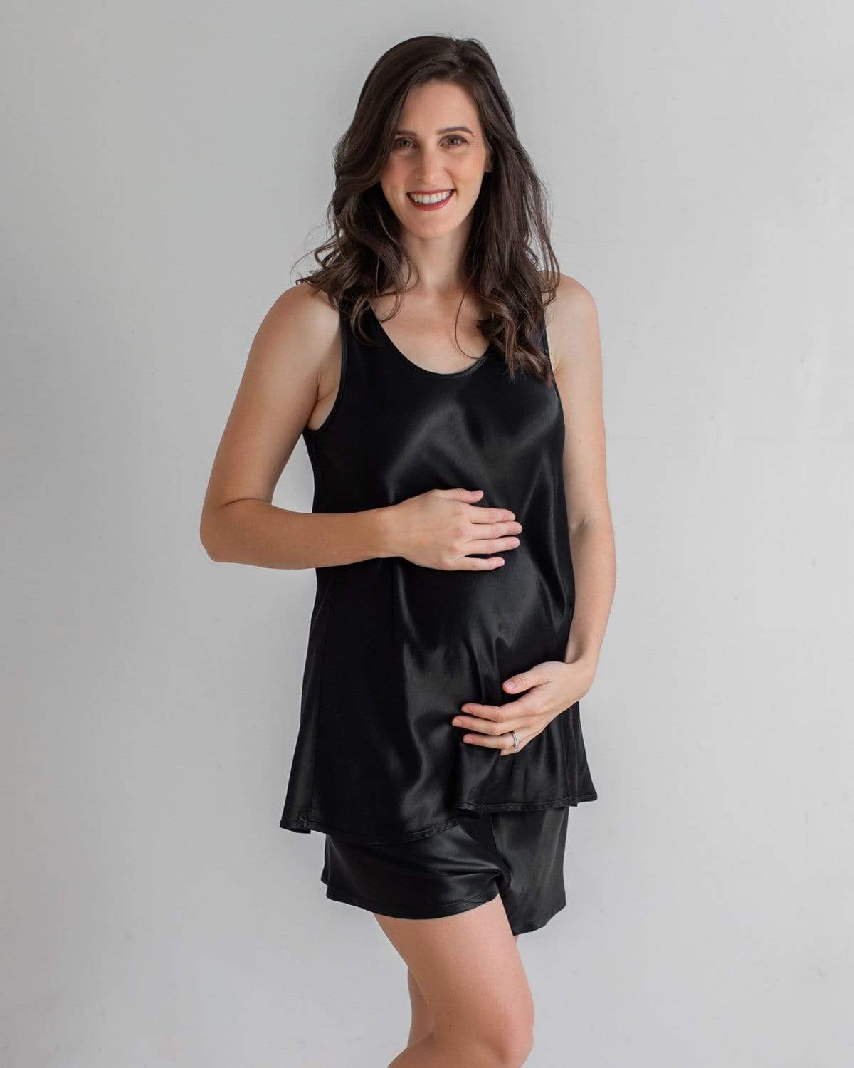 A pregnant woman wearing a white satin maternity sleep tank top and matching pants.