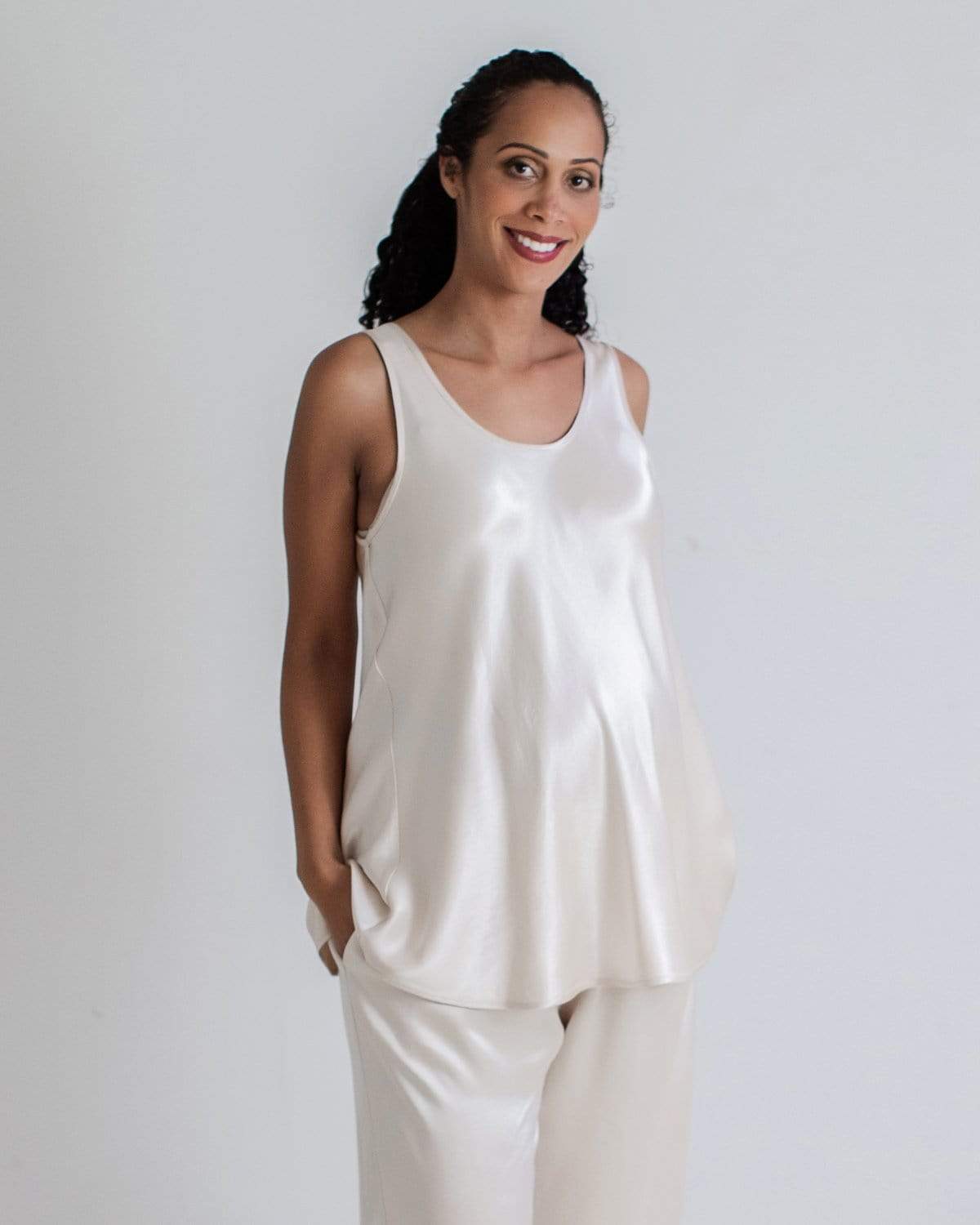 A pregnant woman wearing a white satin maternity sleep tank top and matching pants.